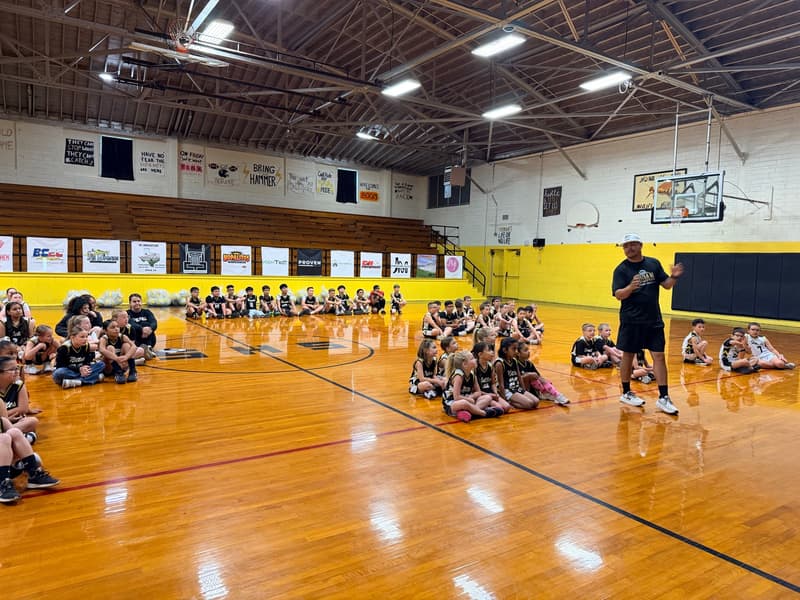 A coach talks to players seated on the gym floor